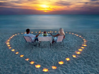 Una pareja cena en una playa a la luz de las velas.