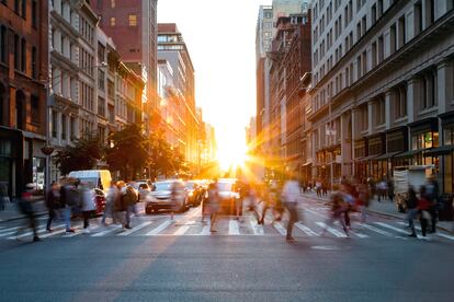 Crowds of busy people walking through the intersection of 5th Avenue and 23rd Street in Manhattan, New York City with bright sunset background.