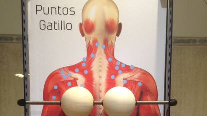 The massage device consists of two wooden balls held in place by a metal rod that is attached to a frame.