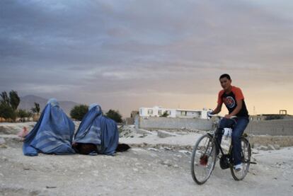 Un joven pasa en su bicicleta junto a dos mujeres ataviadas con burka en el norte de Kabul.