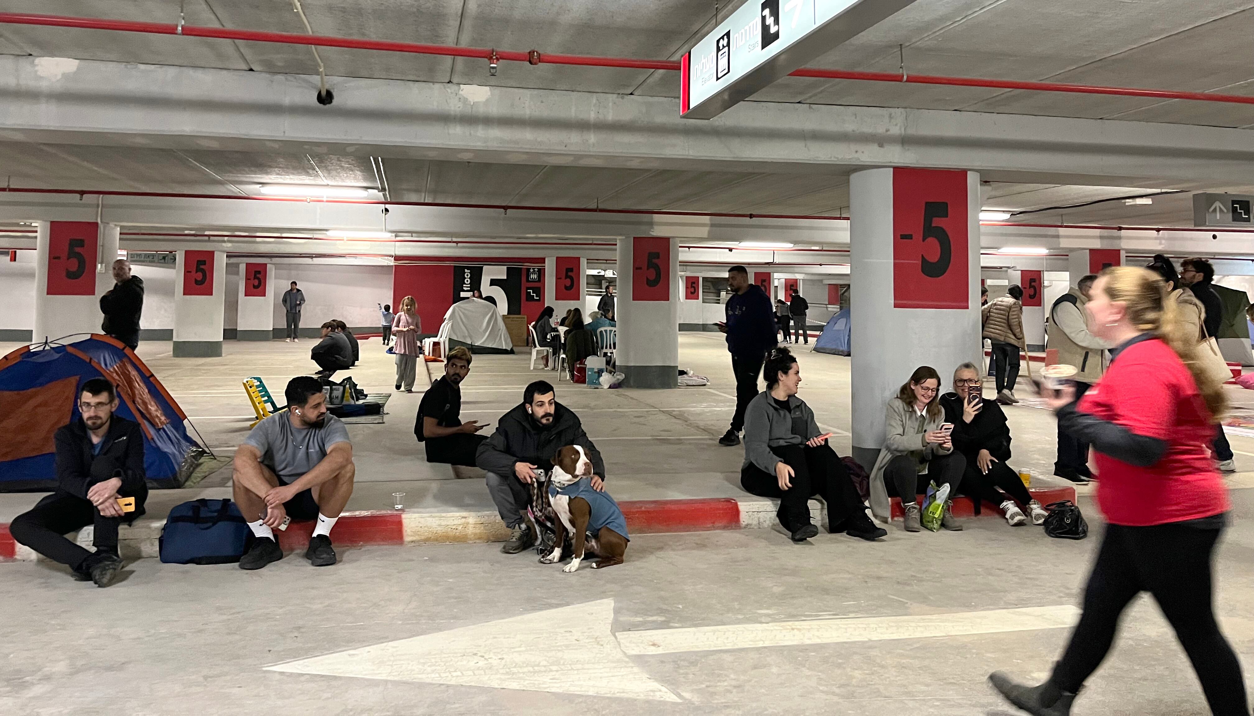 Vecinos de la ciudad israelí de Haifa esperan en el aparcamiento de un centro comercial a que acabe la alerta del ejército israelí por proyectiles, mezclándose con quienes viven ahí permanentemente, el pasado jueves.