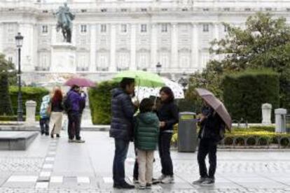 Un turista hace fotos, mientras que los miembros de una familia charlan bajo los paraguas y la lluvia en la Plaza de Oriente de Madrid, con el Palacio Real al fondo. EFE/Archivo