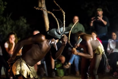 Wame y Tshamiie hacen un baile con cornamentas de algún tipo de ciervo frente a un grupo de turistas.