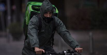 Un 'rider' (repartidor) trabaja bajo la lluvia protegido con un impermeable, en Sevilla.