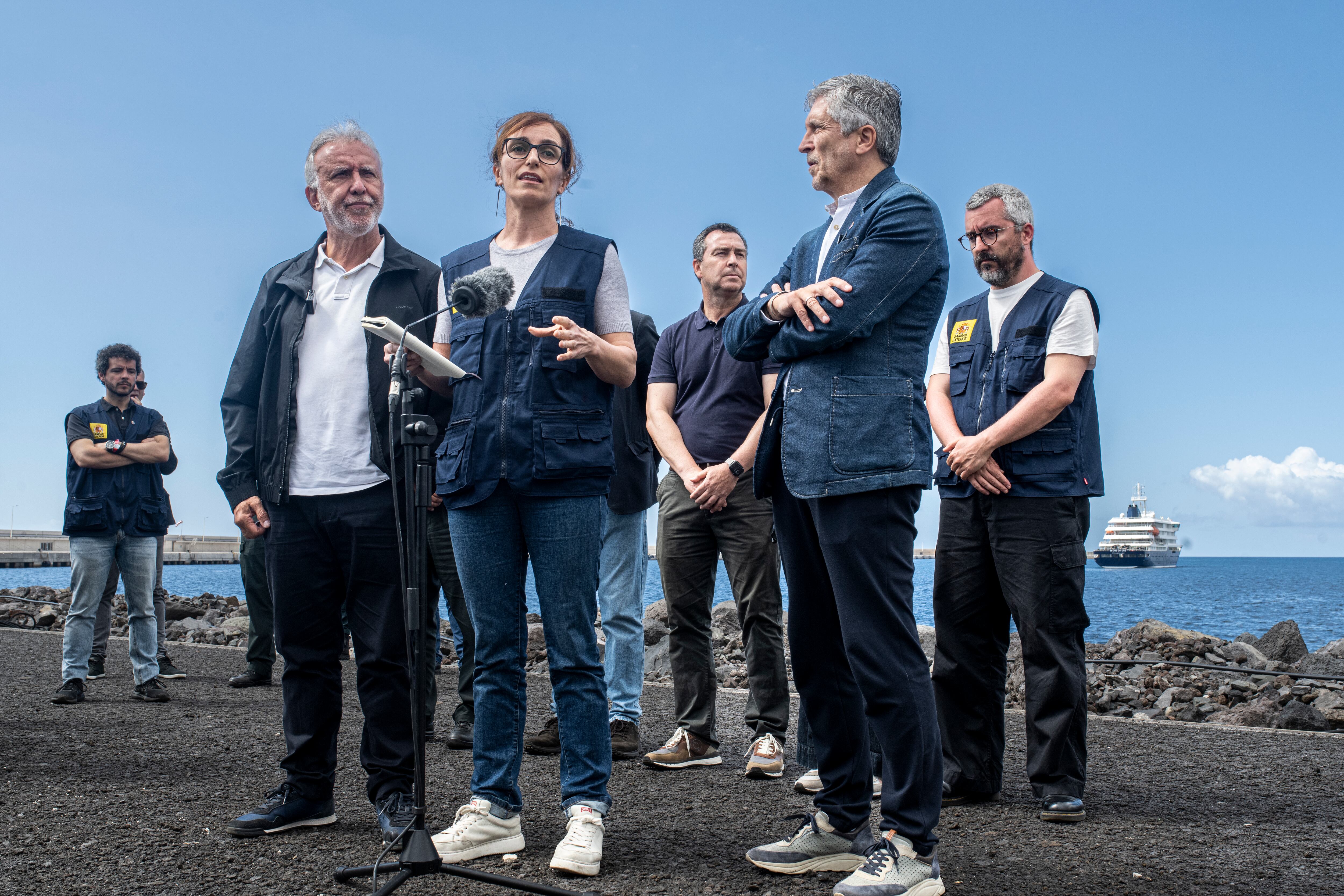 Los ministros de Sanidad, Mónica García (en el centro); Política Territorial, Ángel Víctor Torres (a la izquierda), e Interior, Fernando Grande-Marlaska, en el puerto de Granadilla de Abona. A la derecha, el crucero neerlandés 'MV Hondius'.
