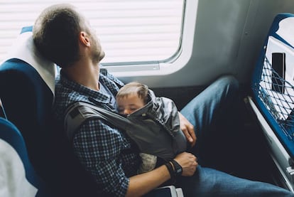 Un padre duerme con su bebé en el tren. 