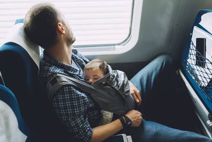 Un padre duerme con su bebé en el tren.