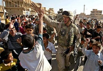 Un <i>marine</i> es saludado ayer por un grupo de niños mientras patrulla por el barrio bagdadí de Sadam City.