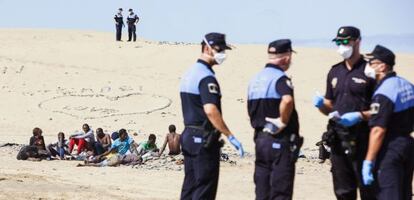 A group of masked police officers watch the immigrants on Maspalomas beach.