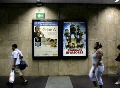 Usuarios del metro de Barcelona pasan, el pasado mes de agosto, junto a un cartel informativo sobre la nueva gripe.