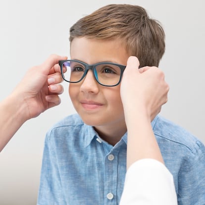 Female optician putting glasses on boy.