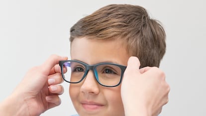 Female optician putting glasses on boy.