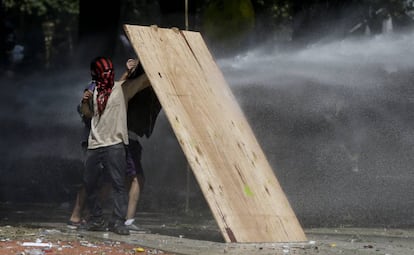 Um grupo de manifestantes tenta conter o jato de água dos agentes com uma placa de madeira.