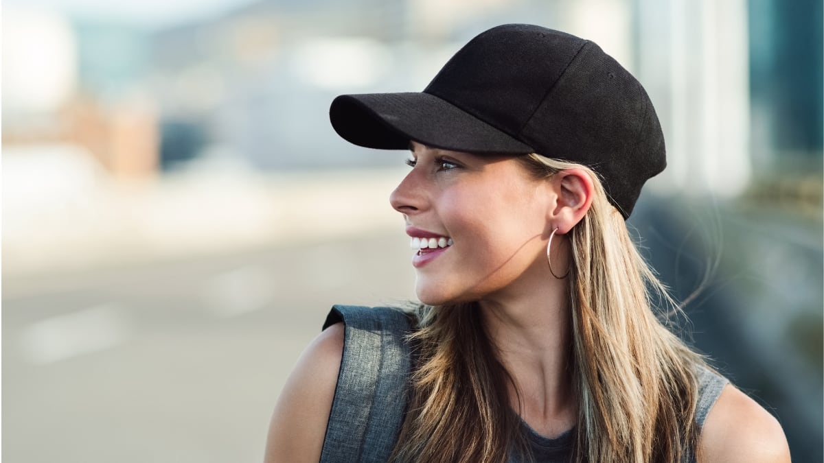 Mujer con gorra negra sonriendo mientras mira hacia un lado.