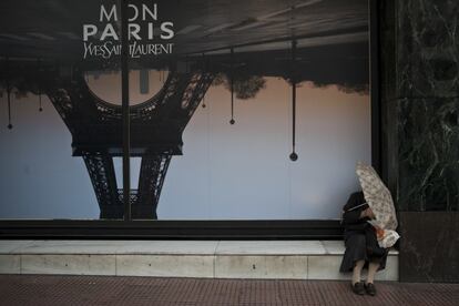 A elderly woman holding an umbrella sits in front of a advertisement depicting the Eiffel Tower, in Athens, Friday, Oct. 28, 2016. (AP Photo/Petros Giannakouris)