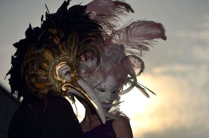 Pôr do sol junto aos canais de Veneza. Duas pessoas mascaradas passeiam pelas ruas da cidade.