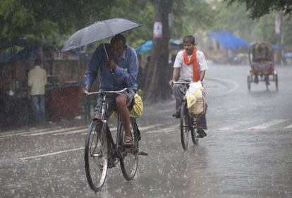 Varios hombres indios andan en bicicleta bajo la lluvia en Allahabad, en plena temporada del monzón en la India.