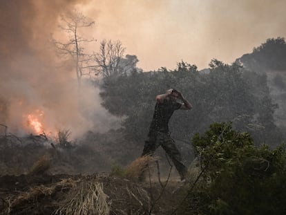 TOPSHOT - A man reacts as a helicopter sprays water at a fire in Gennadi, on the southern part of the Greek island of Rhodes on July 25, 2023, on July 25, 2023, during a wildfire. Wildfires have been raging in Greece amid scorching temperatures, forcing mass evacuations in several tourist spots including on the islands of Rhodes and Corfu. (Photo by Spyros BAKALIS / AFP)