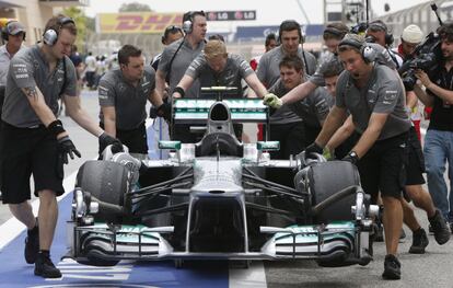 El coche de Lewis Hamilton es empujado por los mecanicos después de reventar la goma de una de las ruedas.