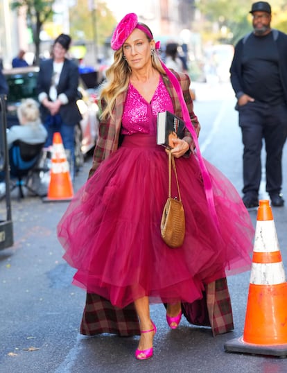Sin atisbo de ironía Carrie Bradshaw usa falda de tul, top de lentejuelas y tocado, todo en fucsia. Para completar, un abrigo de lana de cuadros por encima.