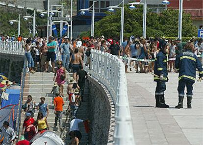 Dos bomberos trabajan en la zona acordonada del paseo marítimo de la playa de Santa Marina, en Ribadesella, rodeados de cientos de personas.