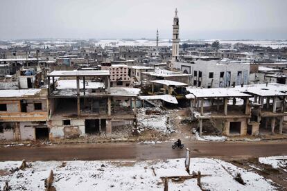 Un hombre sirio monta en moto rodeado de edificios dañados cubiertos de nieve, en Homs (Siria).