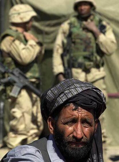Un trabajador afgano espera para comer, ante dos soldados norteamericanos, en la base militar de Kandahar.