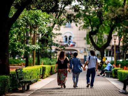 Tres jóvenes pasean por un parque cogidos de las manos.