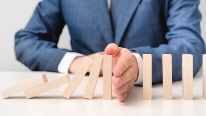 Business risk, crisis effect. Businessman protect falling domino with hand