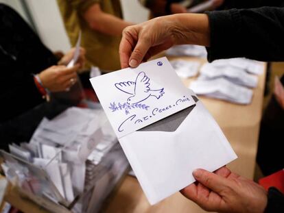 Un miembro de una mesa muestra una tarjeta con una paloma de la paz dentro de un sobre en lugar de una papeleta.