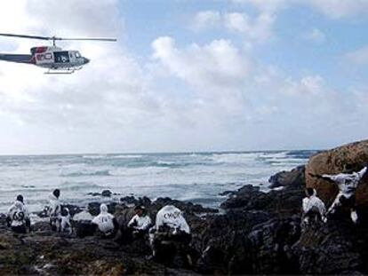 Un helicóptero sobrevuela a un grupo de soldados que limpia chapapote cerca de Carnota.