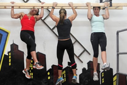 Three women hoping to become firefighters train in a gym, in order to pass the difficult physical tests.