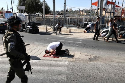 Un miembro de la seguridad israelí pasa junto a un musulmán que participa en la oración de los viernes en el barrio de Ras al Amud, en Jerusalén.