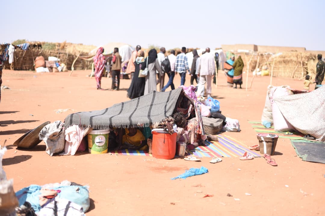 Un grupo de desplazados internos llegados a la ciudad de El Obeid, en Kordofán del Norte, Sudán, con escasas pertenencias y resguardándose del sol debajo de una tela, en junio de 2026. Imagen de Issam Mukhtar, voluntario de la iniciativa local de desarrollo comunitario Kiyan.