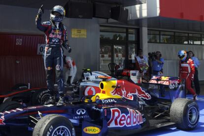 Vettel festeja el triunfo, mientras Alonso pasa tras él cabizbajo.
