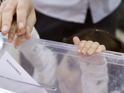 Un padre empuja el voto con el dedo de su pequeña hija en el colegio electoral en Madrid.