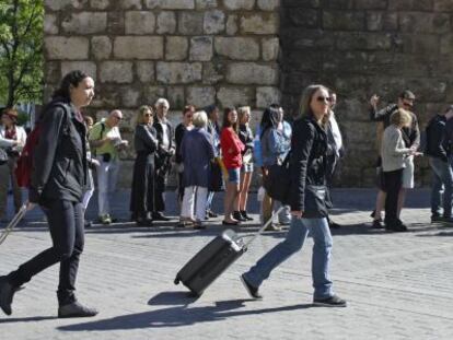 Dos mujeres pasan con sus maletas junto al Alcázar de Sevilla.