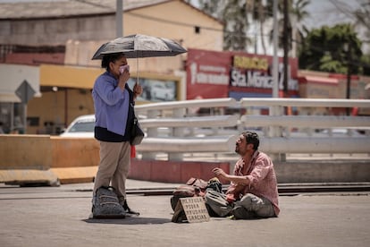 Sentado en el concreto caliente, un hombre en situación de calle pide apoyo a una mujer que se limpia el sudor en medio de una ola de calor en Mexicali (México), el pasado 14 de junio. 