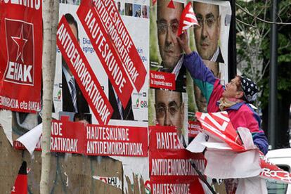 Un mujer arranca los letreros con el lema <i>Elecciones antidemocráticas</i> pegados sobre carteles de propaganda electoral en las calles de Bilbao.