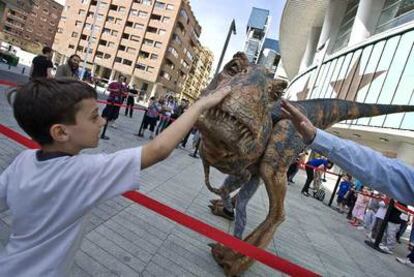 Un niño toca una de las maquetas utilizadas en el espectáculo <i>Caminando entre dinosaurios,</i> delante del Palacio de Deportes.