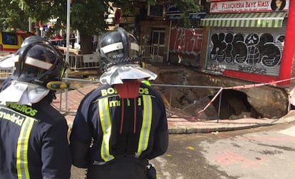 Dos bomberos observan el socavón de la avenida del Marqués de Corbera.