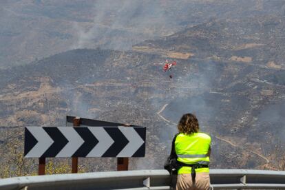 El Centro Coordinador de Seguridad y Emergencias (Cecoes) 112 del Ejecutivo regional informa de que nueve helicópteros y un avión a las tareas de extinción se incorporarán este domingo a la lucha contra el fuego. En la imagen, una mujer observa los trabajos de extinción del incendio.