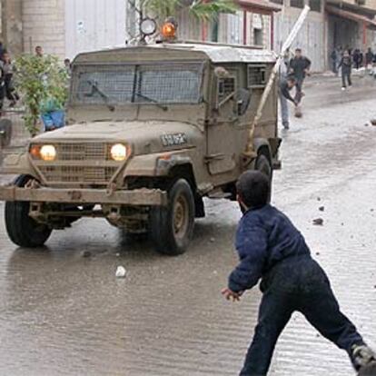 Un niño palestino lanza piedras contra un vehículo militar israelí, ayer, en Kalkilia.