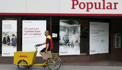 Un repartidor pasa ante una oficina del Banco Popular en el Paseo de Gracia esquina con la calle Aragón de Barcelona.
