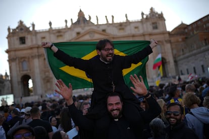 Dos clérigos celebran la fumata blanca blandiendo la bandera de Brasil.
