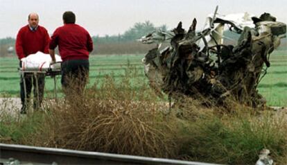 Personal del tanatorio retira el cadáver del fallecido junto a los restos del vehículo accidentado.