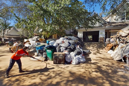 Una voluntaria de una ONG cristiana barre el lodo de una carretera ante pilas de basura creada por el huracán Helene. 