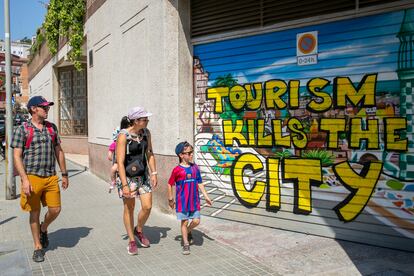 A family of tourists walk in front of a graffiti against tourism on July 18, 2022 in Barcelona, Spain