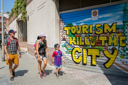 A family of tourists walk in front of a graffiti against tourism on July 18, 2022 in Barcelona, Spain