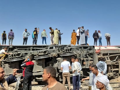 Un grupo de personas sobre un vagón volcado en un accidente de tren en la provincia egipcia de Sohag toman imágenes con sus teléfonos, mientras otros inspeccionan la escena.